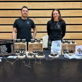 Customer Gamanity Man and Woman standing behind table of products