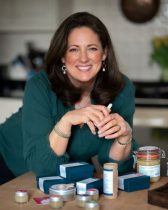 Customer Tam Mason Woman leaning on a desk with cosmetic products in jars and boxes in front of her